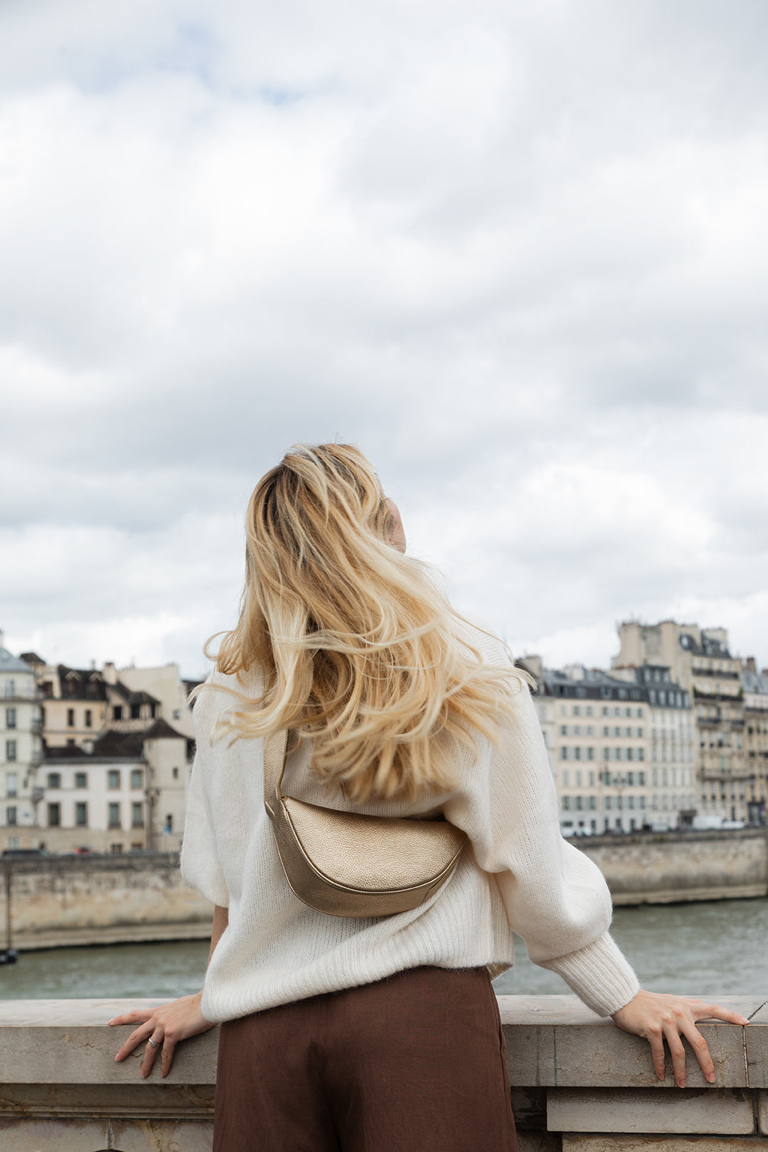 Femme portant le mini sac banane Lou ENVOL doré au bord de l'eau #Couleur_Gold