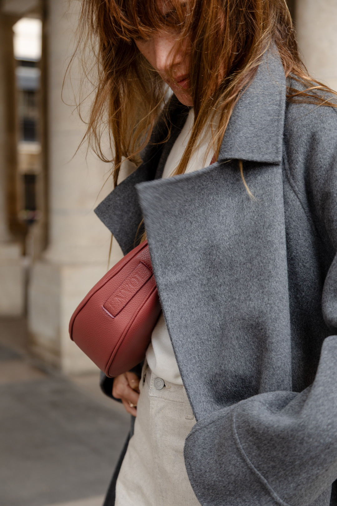 Femme portant le mini sac banane Lou ENVOL bois de rose avec un manteau gris, de profil #Couleur_Bois de Rose