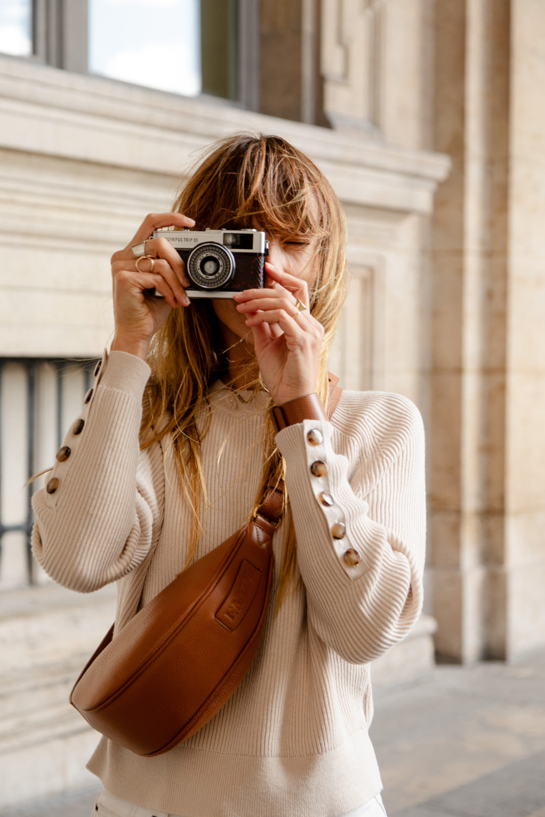 Femme portant le mini sac banane Lou ENVOL camel avec un appareil photo #Couleur_Camel